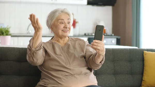Старшая Женщина Улыбается Делает Видеозвонок Родственниками Смотрит Камеру Машет Сидит — стоковое фото