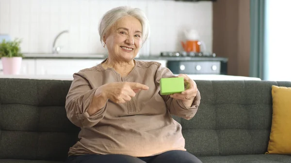 Ηλικιωμένη Γυναίκα Κρατάει Κάτι Πράσινο Στην Πολυθρόνα Της Δείχνοντας Ένα — Φωτογραφία Αρχείου