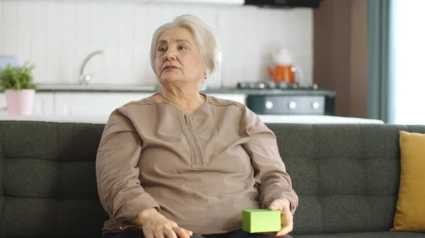 Ηλικιωμένη Γυναίκα Κρατάει Κάτι Πράσινο Στην Πολυθρόνα Της Δείχνοντας Ένα — Φωτογραφία Αρχείου