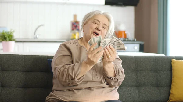 老年妇女坐在客厅的沙发上数着钞票 计算着美元 预算支票 退休金 快乐的老年妇女数着美元钞票 — 图库照片
