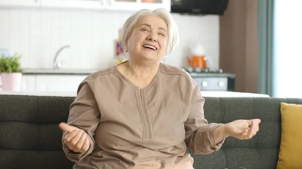 安详的老妇人在安静的家里休息 寂寞的老妇人一个人坐在沙发上 安安静静地呆在家里 对着屏幕上方空旷的广告空间微笑 快乐老妇人的画像 — 图库照片