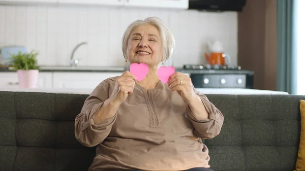 Mutlu Yaşlı Kadın Gözlerinden Iki Küçük Pembe Kağıt Kalp Tutuyor — Stok fotoğraf