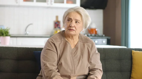 可怜的老妇人在家里或养老院里 老年人保健服务 老太婆坐在客厅沙发上 看着屏幕右侧空旷的广告空间的画像 — 图库照片