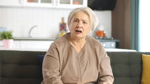 一位白发苍苍的老妇人正在和另一个人在网上视频通话中争吵 愤怒的老年妇女在家里客厅的沙发上用笔记本电脑进行视频通话 前视镜 — 图库照片