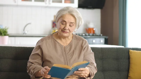 Elderly woman in her peaceful home reading a book, enjoying her free time. Happy old people, retired woman concept. Concept of love to read books.