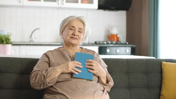 White-haired old woman holding an old novel book on her chest. Woman who loves the old classic novel book she is reading.Concept of people who love to read.Hobby.Happy seniors, retired woman concept.