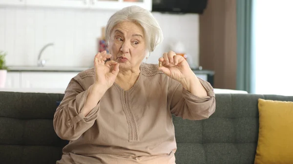一位白发苍苍的老妇人指着客厅沙发上的一颗药丸 她指出手中的药是完美的 快乐的老妇人表现出医疗保健 疾病治疗 维生素 — 图库照片