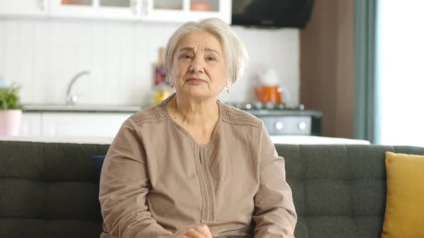 有思想的老妇人在家里或养老院里 老年人保健服务 老年妇女坐在客厅沙发上看着相机的画像 — 图库照片