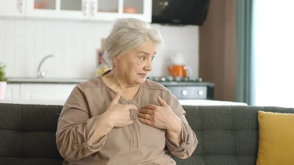 头发灰白的老年妇女穿着休闲装 疑神疑鬼 满脸不赞成的表情 消极的人 暴躁的老妇人坐在家里的沙发上 — 图库照片