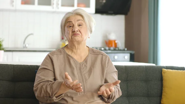 头发灰白的老年妇女穿着休闲装 疑神疑鬼 满脸不赞成的表情 消极的人 暴躁的老妇人坐在家里的沙发上 — 图库照片