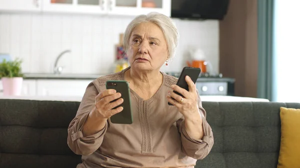 老妇人看着她的社交媒体账户 阅读新闻 用两部智能手机留言 老妇人试图用两台智能手机对着摄像机 看着空荡荡的广告空间 — 图库照片