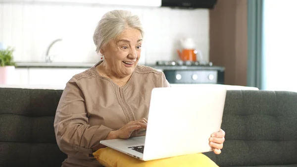 年长的成熟女人在笔记本电脑上花时间上网 一位70多岁的妇女正在通过虚拟聊天进行视频通话 老太太在客厅沙发上网上购物 — 图库照片