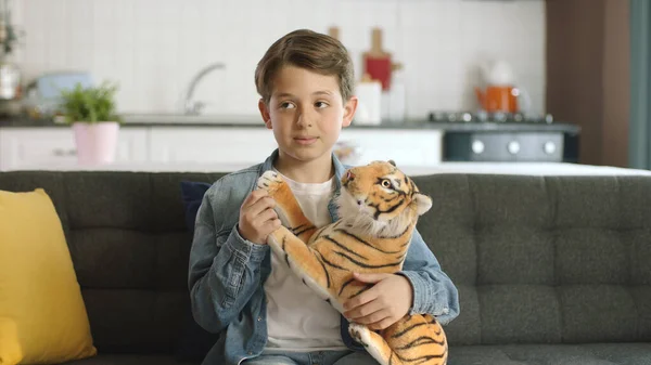 Home alone,friendless little boy plays with toy tiger.Brown toy tiger in child\'s hand.Child playing with a toy tiger,looking at the empty advertising space to the left of the screen in the living room
