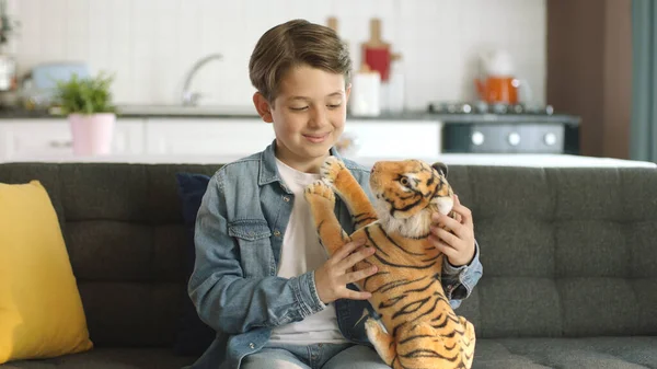 Home alone, little boy without friends plays with a toy tiger.Brown toy tiger in child\'s hand. Child playing with a toy tiger in the living room.