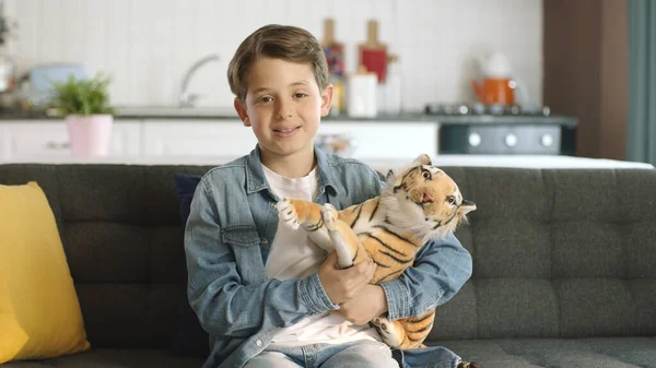 Home alone, friendless little boy plays with toy tiger. Brown toy tiger in child's hand. Boy playing with toy tiger in living room smiling at camera.