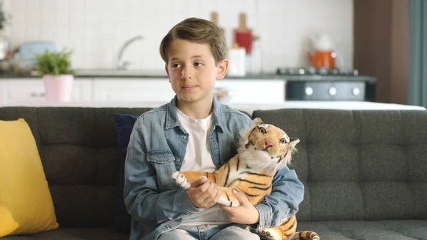 Home alone,friendless little boy plays with toy tiger.Brown toy tiger in child\'s hand.Child playing with a toy tiger,looking at the empty advertising space to the left of the screen in the living room
