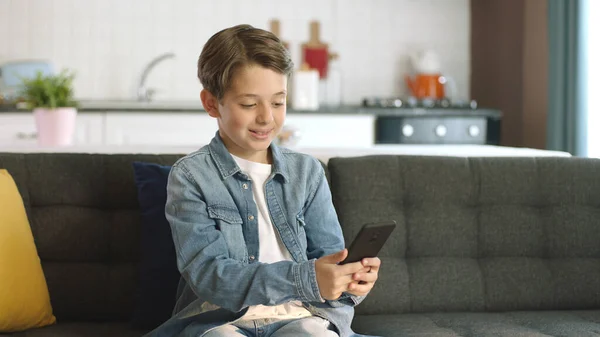 stock image Friendly little boy making a video call on his cell phone. Little funny boy making online video call with friends on smartphone while sitting on sofa at home.