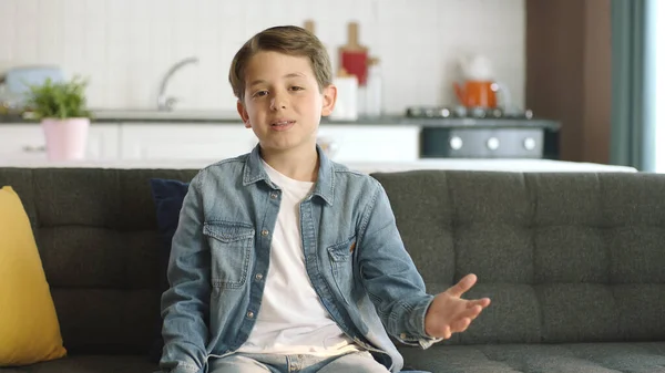 stock image Portrait of a bored sad boy at home.Lonely and bored boy sitting alone on sofa at home, talking to himself. Feeling depressed and sad. People and negative emotions concept.