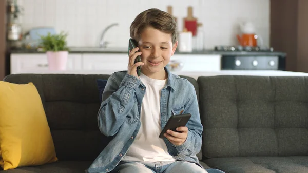 stock image Technology addicted little boy.Curious boy sitting on sofa and playing games with 2 smartphones. The little boy is surfing the internet at home, talking to his friend on one of his mobile phones.