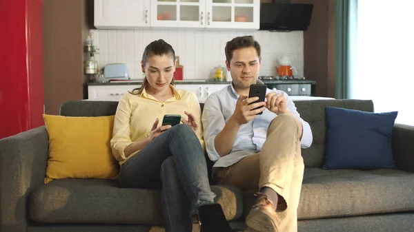 소파에 앉아서 사용하여 스마트폰을 보면서 이야기하지 부부들이 있습니다 온라인 쇼핑을 — 스톡 사진