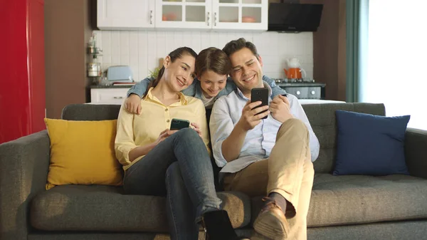 Happy adult parents with cute kids looking at phone screen having fun with technology together. Technology addicted family having fun with smartphone.
