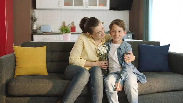 Little boy surprise his mother with a gift on Mother\'s Day. Happy family portrait. Little boy giving flowers to his mother at home as a birthday or mother\'s day gift.