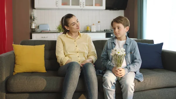 Little boy surprise his mother with a gift on Mother\'s Day. Happy family portrait. Little boy giving flowers to his mother at home as a birthday or mother\'s day gift.