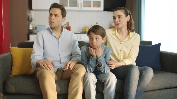 Happy Caucasian family sitting on comfortable sofa and looking at empty advertising space to the left of the camera. Happy family portrait.