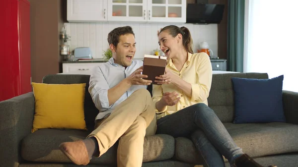 Woman Surprises Her Young Husband Giving Gift Wrap While Watching — Stock Photo, Image