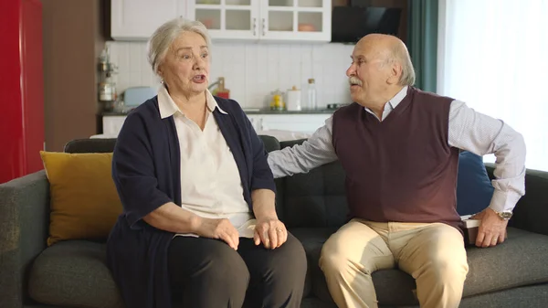 An elderly couple sitting in their armchair at home and arguing, getting angry with each other. Image of an elderly couple in troubled marriages. Problems experienced by married couples.