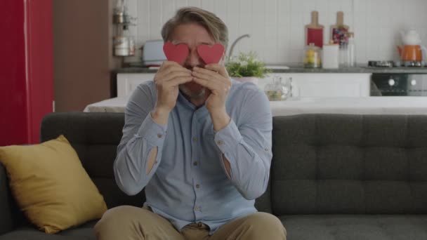Gözlerinde Iki Kağıt Kalple Oynayan Mutlu Adamın Videosu Evinin Kanepesinde — Stok video