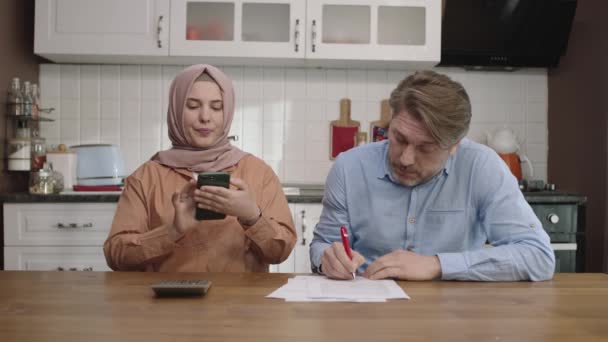 Man Zijn Hijab Geklede Vrouw Berekenen Aan Keukentafel Het Echtpaar — Stockvideo