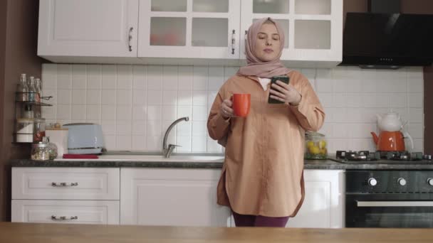 Mosolygó Nézi Receptek Miközben Iszik Kávét Konyhában Fiatal Hidzsáb Gazdaság — Stock videók