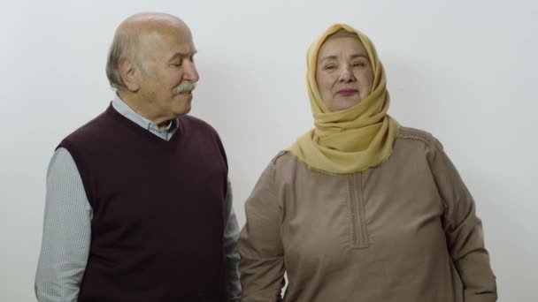 カメラで微笑むヒジャーブの幸せ老女とその夫 白地に孤立した高齢夫婦のポートレート — ストック動画