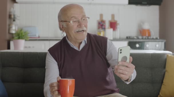 Staruszek Ogląda Zabawny Filmik Swoim Smartfonie Pijąc Kawę Domu Człowiek — Wideo stockowe