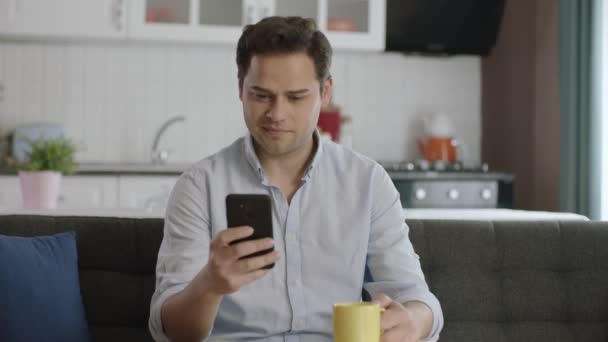 这位用户一边喝咖啡 一边在智能手机上浏览社交媒体账户 他对自己看到的新闻或信息感到惊讶和微笑 — 图库视频影像