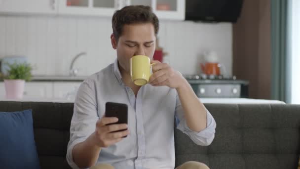 Nachdenklicher Junger Mann Der Sein Smartphone Benutzt Und Hause Kaffee — Stockvideo