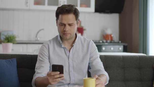 Lächelnder Junger Mann Der Sein Smartphone Benutzt Und Hause Kaffee — Stockvideo