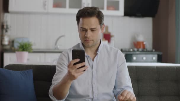 Casual Ντυμένος Νεαρός Άνδρας Χρησιμοποιώντας Smartphone Στον Καναπέ Στο Σπίτι — Αρχείο Βίντεο