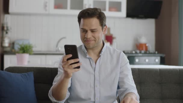 Smuk Spændt Ung Mand Sidder Sofaen Derhjemme Viser Smartphone Skærm – Stock-video