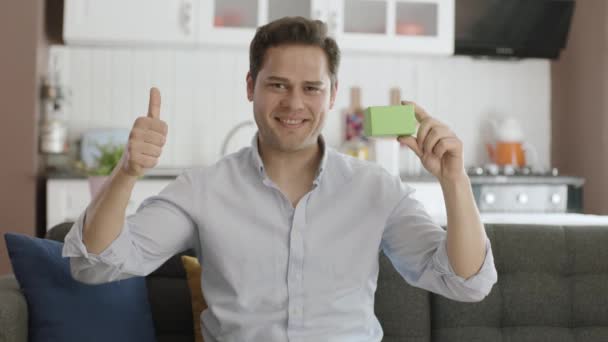 Joven Hombre Guapo Caucásico Sosteniendo Algo Verde Mostrando Producto Sonriendo — Vídeo de stock