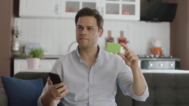 Hombre Sosteniendo Teléfono Inteligente Algo Verde Sofá Mostrando Producto Sonriendo — Vídeo de stock
