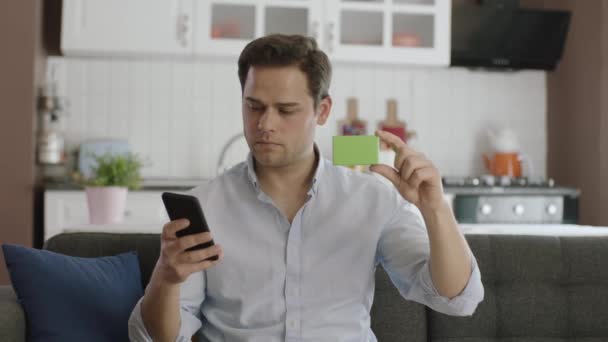 Hombre Sosteniendo Teléfono Inteligente Algo Verde Sofá Mostrando Producto Sonriendo — Vídeo de stock
