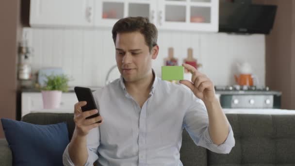 Man Håller Smartphone Och Något Grönt Sin Soffa Visar Produkt — Stockvideo