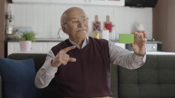 Yaşlı Adam Kanepede Elinde Yeşil Bir Şey Tutuyor Ürünü Gösteriyor — Stok video