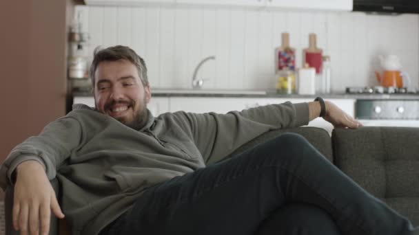 快乐的年轻人在他的新公寓里笑着 放松的微笑着坐在客厅沙发上的年轻人 幸福家庭的概念 — 图库视频影像