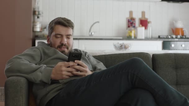 年轻人躺在沙发上看着智能手机 使用智能手机 浏览社交媒体账户 发短信或观看视频 — 图库视频影像