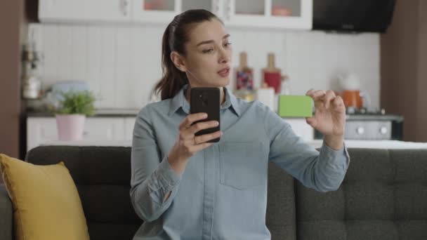 Mujer Sosteniendo Smartphone Caja Verde Sofá Mostrando Producto Sonriendo Presentando — Vídeo de stock