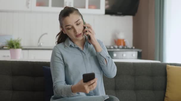 忙碌的女商人用两个智能手机努力工作 年轻的自由职业者女人在家里用一个电话聊天 在另一个电话上网 她在努力跟上网上订单 — 图库视频影像