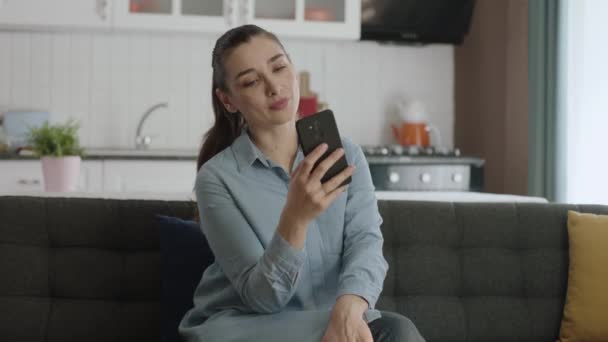 若い女性は自宅でソファに座っている間 携帯電話でインターネットを閲覧する時間を過ごす眼鏡の若い女性 — ストック動画